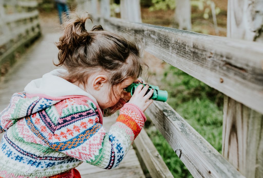 A curious child engaging in bird watching, peering through binoculars with enthusiasm.